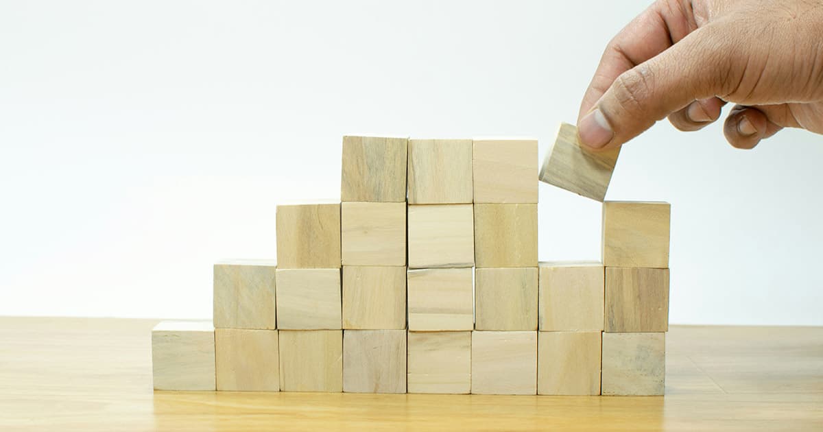 A hand placing a block on top of a stack of wooden blocks