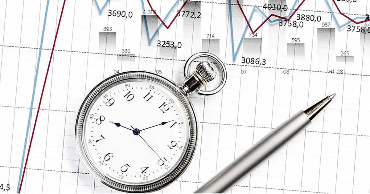 A stopwatch, silver pen, and financial charts with numbers and line graphs, symbolizing time management and financial analysis, are displayed on a white background.
